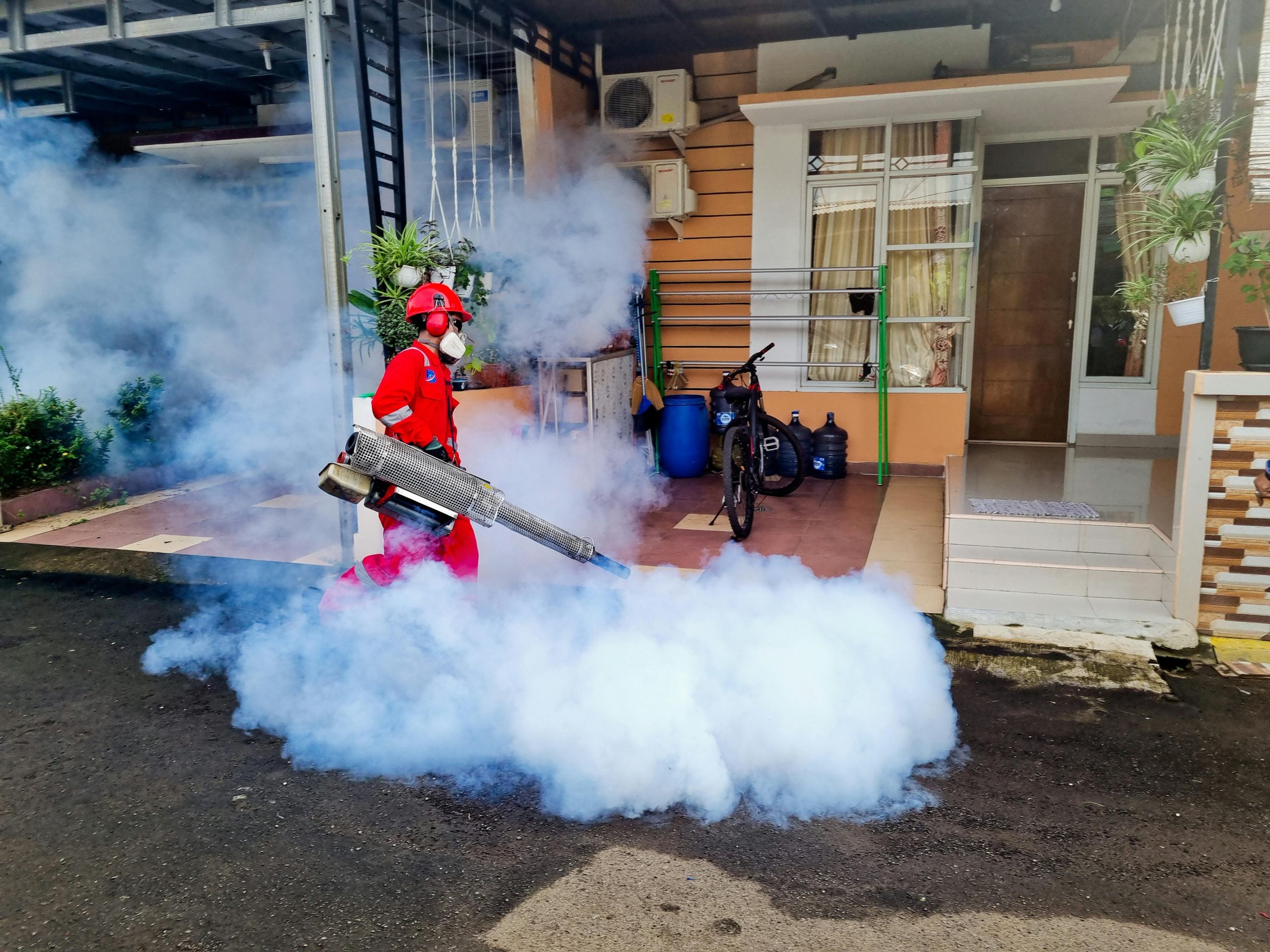 Pest control specialist using a smoke machine to fumigate outside a house.