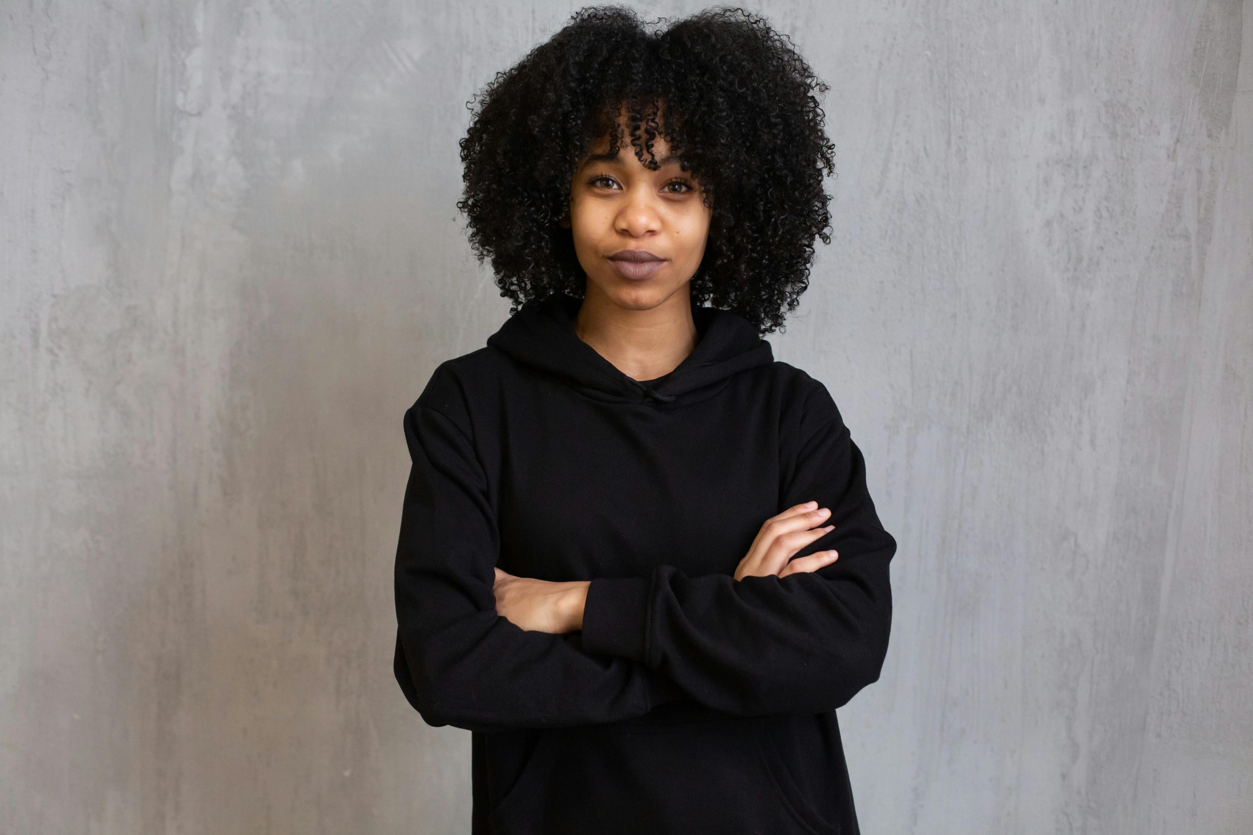 Young African American female with Afro hairstyle wearing casual clothes standing with crossed arms and looking at camera
